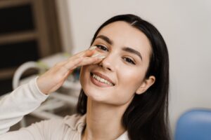 Smiling woman gently touching her nose with her fingertips, happy with her progress during rhinoplasty recovery